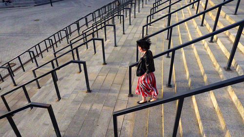 Full length of woman wearing striped skirt and jacket on steps amidst railing in city