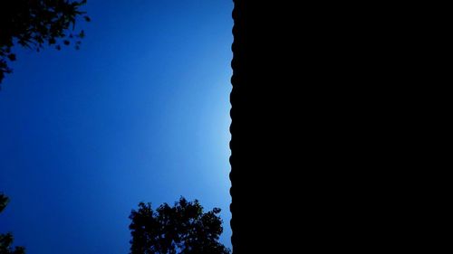 Low angle view of silhouette trees against clear blue sky