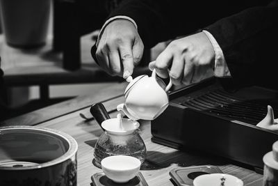 Cropped image of hands pouring tea in pot on table