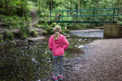 Rear view of girl standing by stream in forest