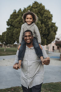 Joyful son sitting on happy father's shoulders at park playground