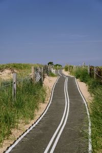 Road amidst field against clear blue sky