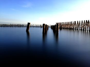 Wooden posts in sea against sky