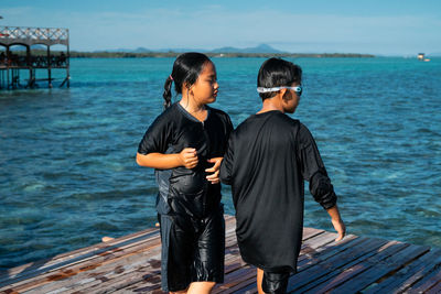 Boy and girl standing on pier over sea against sky