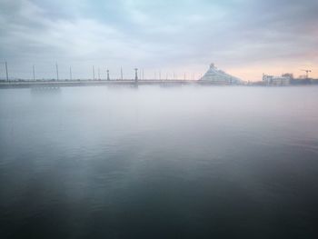 View of city at waterfront against cloudy sky