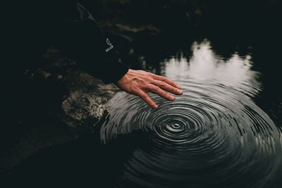 Cropped image of hand over rippled water in lake