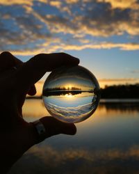 Reflection of hand holding glass against sky during sunset