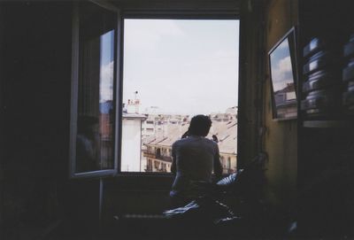 Rear view of man smoking and talking on mobile phone at window