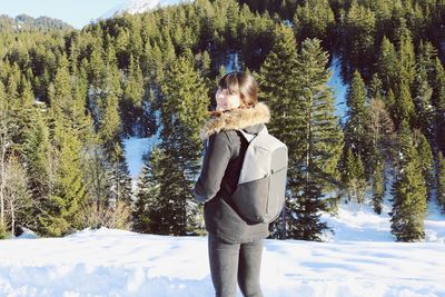 Rear view portrait of young woman standing in forest during winter