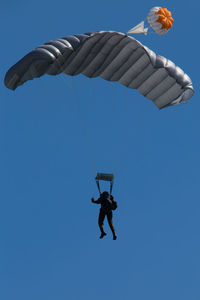 Low angle view of man paragliding against clear blue sky