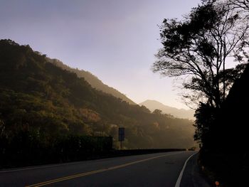 Road by silhouette trees against sky in city