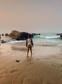 Rear view of boy standing on beach against sky