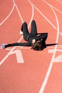 High angle view of tired woman lying with water bottle on running track