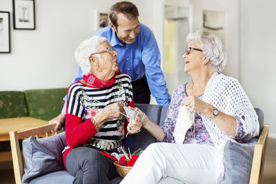 Senior woman talking to man while knitting at nursing home