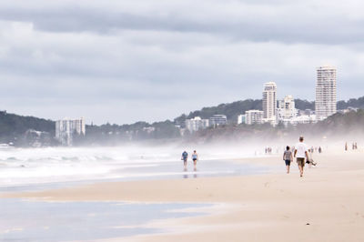 People walking at beach against cloudy sky