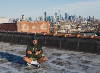 Full length portrait of man sitting against buildings in city