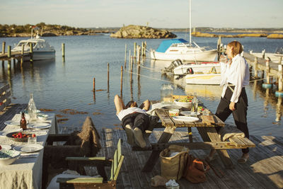 Side view of woman looking at man lying at harbor on sunny day