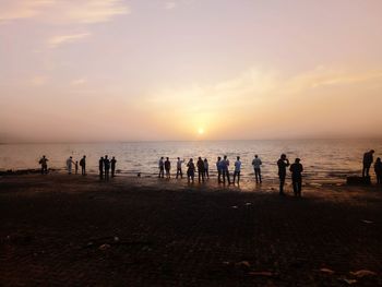 Silhouette people on beach against sky during sunset