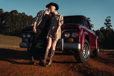 Young couple in love sitting in red vintage pickup and kissing in sunset in summer