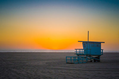 Lifeguard hut on beach against clear sky during sunset