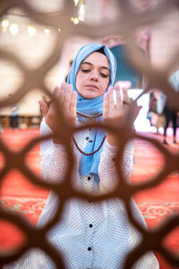 Young woman praying in mosque seen through window fence