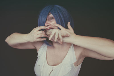 Digital composite image of woman with hand in mouth standing against black background