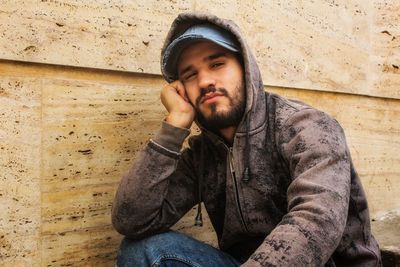 Portrait of young man sitting against wall