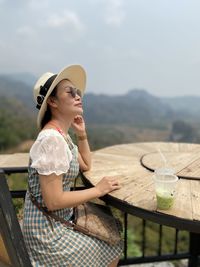Full length of woman wearing hat sitting on table against mountains