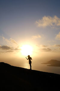 Silhouette man standing on shore against sky during sunset