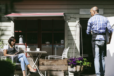 Man walking towards cafe looking at female colleague working on digital tablet