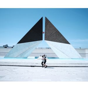 Man and woman walking on umbrella against clear sky