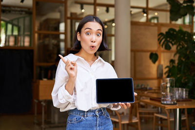 Portrait of young woman using mobile phone while standing in cafe