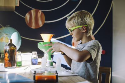 Ambitious male student mixing chemical through funnel at table