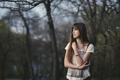 Thoughtful woman standing against bare trees at park