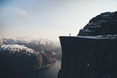 Man on cliff by river against sky during winter