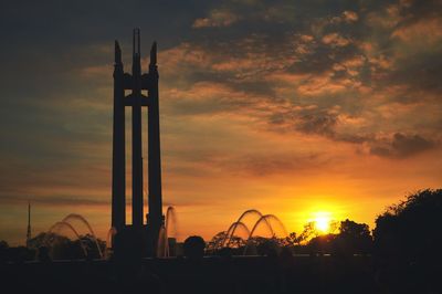 Low angle view of silhouette quezon memorial circle against cloudy sky during sunset