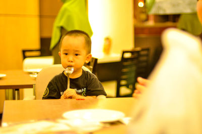 Boy holding spoon while sitting in restaurant