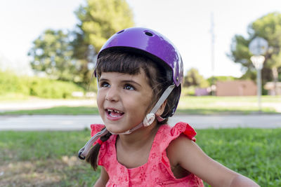 Little girl looking at camera while wearing protective helmet outdoors in a park.