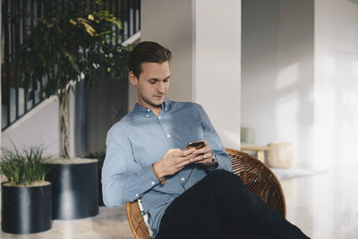 Businessman using smart phone while sitting on chair in office