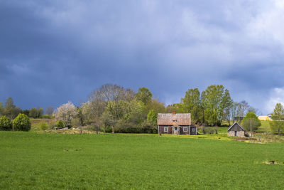House on field by trees against sky