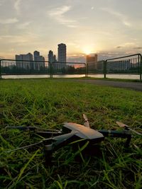 Woman on grass in city against sky during sunset