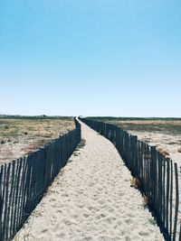 Wooden footpath leading towards beach against clear blue sky