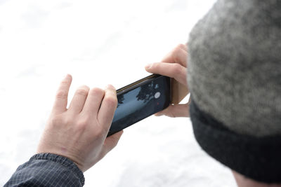 Close-up of man holding mobile phone against sky