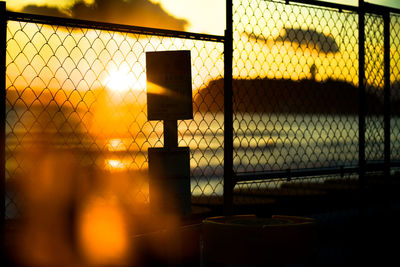 Sign board by chainlink fence by sea during sunset