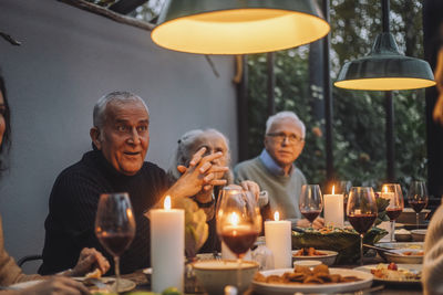 Mature man with hands clasped sitting by male and female friends at dinner party