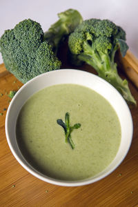 Cream of broccoli soup in a white bowl on a wooden table with slices of the stems