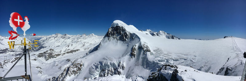 Panoramic view of snowcapped breithorn mountains and wind vane against clear blue sky