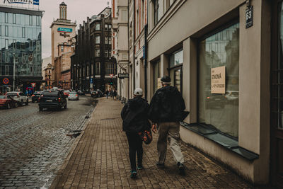 Rear view of men walking on street amidst buildings in city