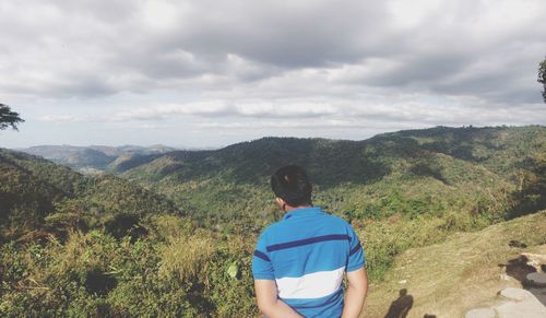 Rear view of man standing on mountain against cloudy sky