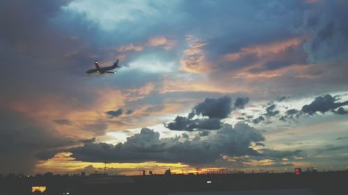 Airplane flying over dramatic sky during sunset